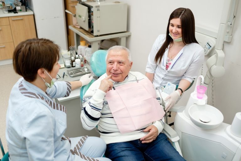 Dentist And Nurse Making Professional Teeth Checkup Male Senior Patient At The Dental Office. Dental Care For Older People. Dentistry, Medicine And Health Care Concept